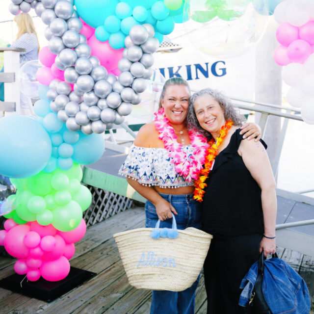 Two women standing next to a balloon arch on a dock.