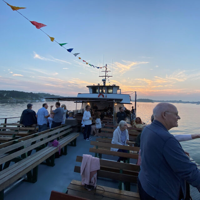 A group of people standing on the deck of a boat at sunset.