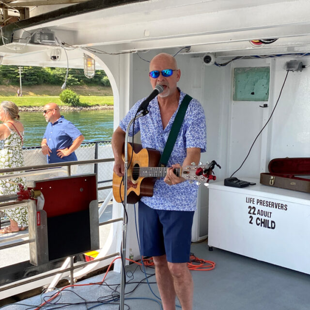 A man singing on a boat with a guitar.