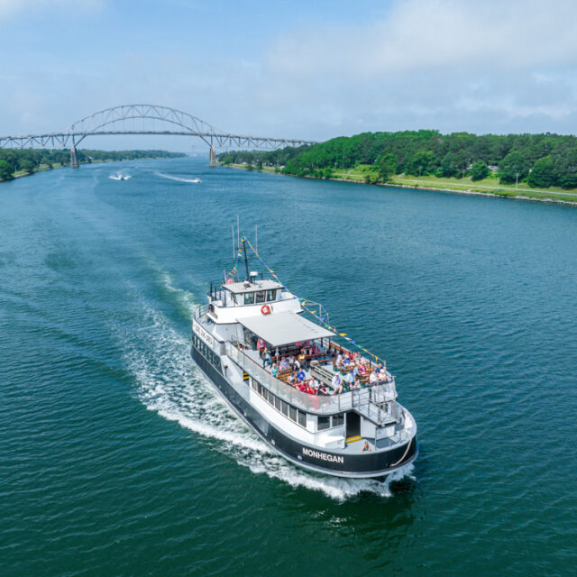 A boat traveling down a river with a bridge in the background.