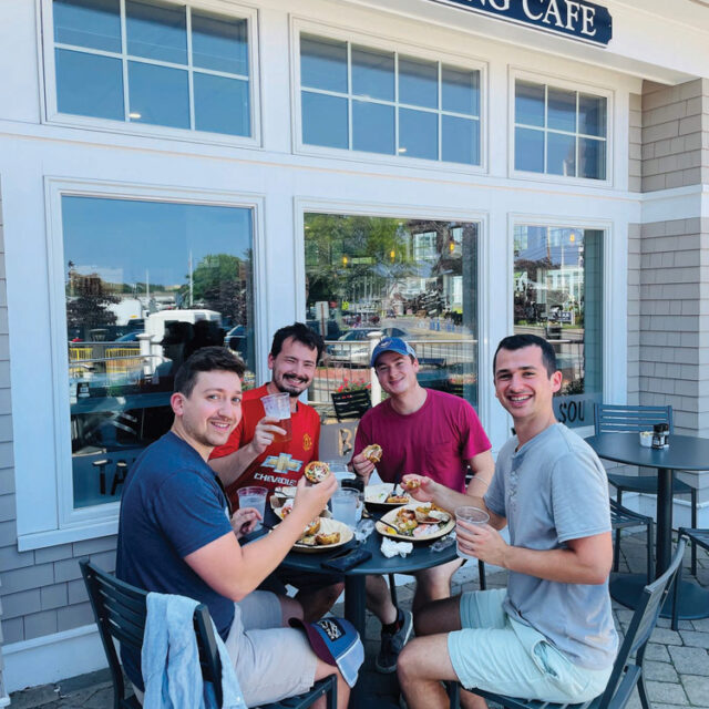 A group of men sitting at a table outside of the landing cafe.