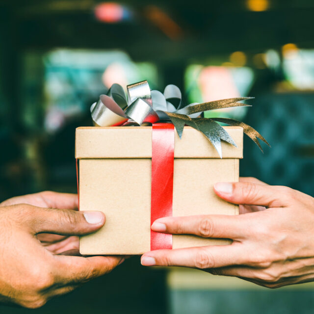 Two hands giving a gift box to each other.