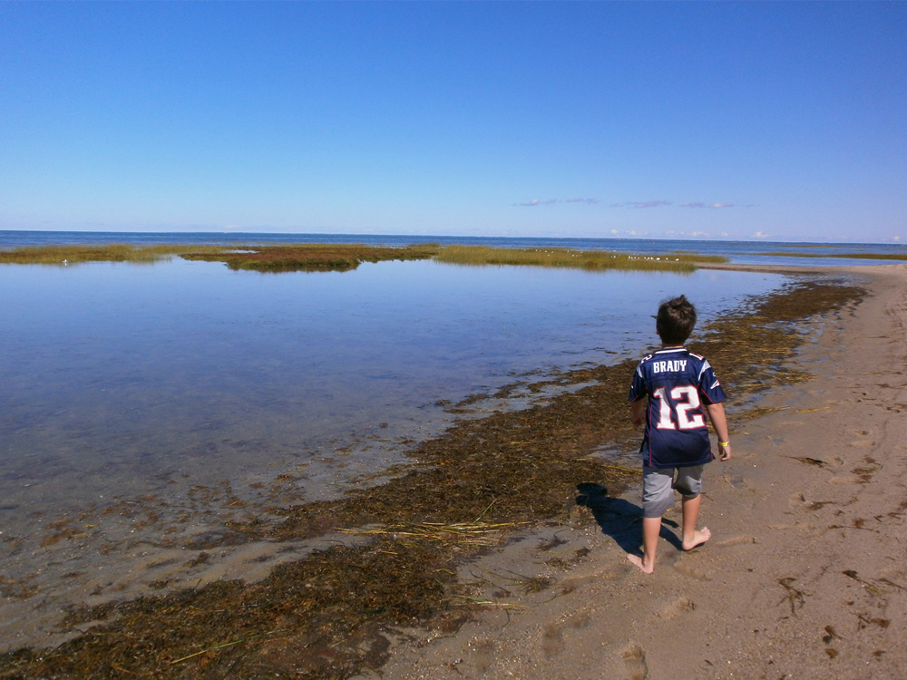 young child walking along the beach with a Tom Brady football shirt on